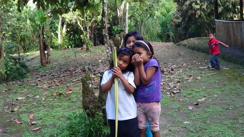 Four children from the Kichwa Amazon tribe. One girl whispers to another friend while another girl stands behind. Young boy tries to act up in the background