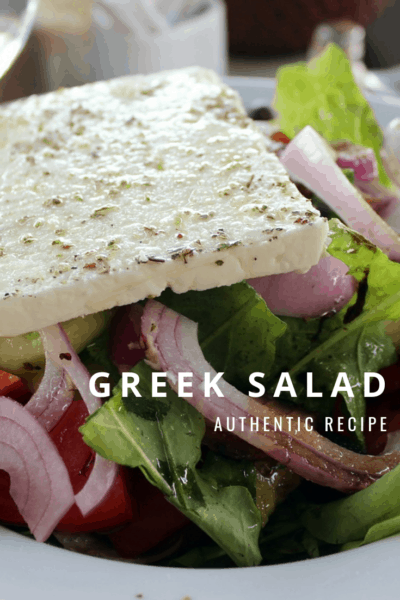 closeup of a bowl of Greek salad with slab of feta cheese. text overlay says Greek salad authentic recipe.