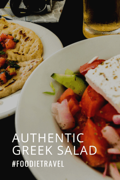 A bowl of Greek salad, plate of bread and glass of beer. Text overlay says Authentic Greek Saladl #foodietravel