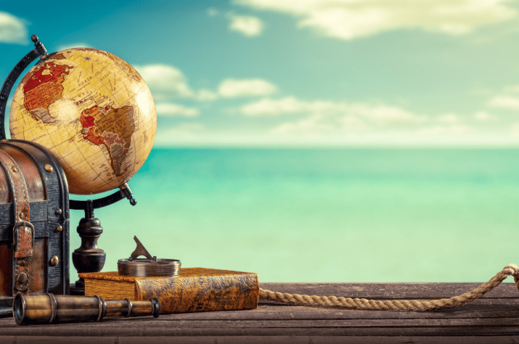 vintage globe, suitcase, roe, telescope on a pier with ocean in the background