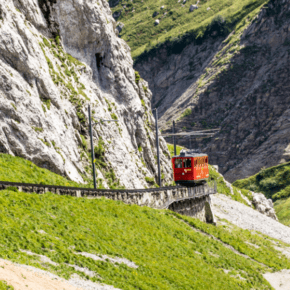 Red train goes down the track on Mount Pilatus. Text block says Steepest cogwheel train in the world