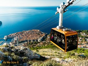 Orange cable car rises to top of Mount Srd. View of Dubrovnik and Adriatic sea in background.