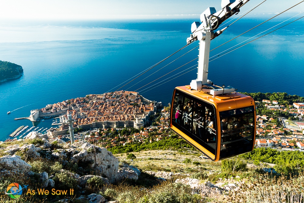 Orange cable car rises to top of Mount Srd. View of Dubrovnik and Adriatic sea in background.