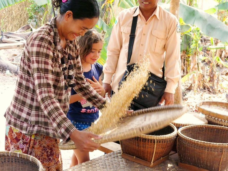woman smiling as she flips rice for a couple of visitors