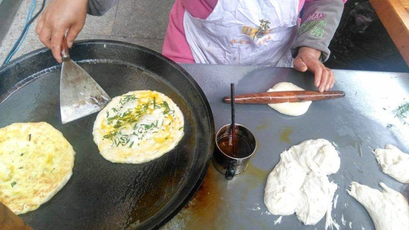 hand holding a spatula, preparing to remove a round egg omelette sprinkled with herbs from a grill