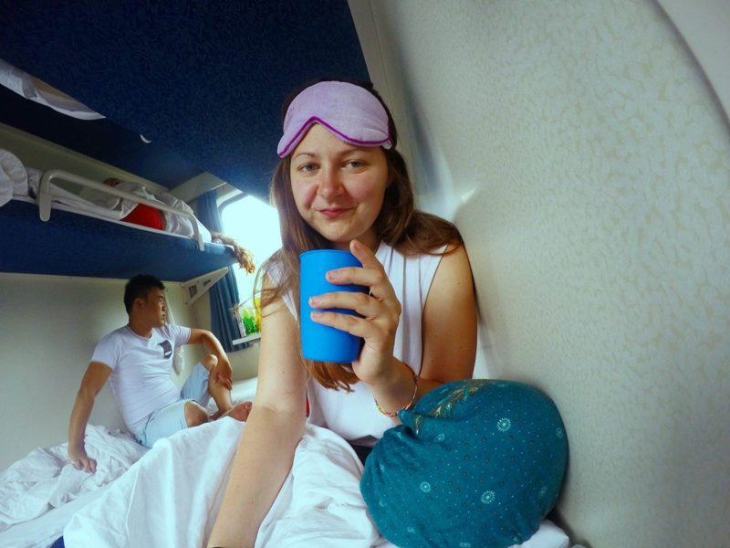 selfie of author on a train bunk holding a blue plastic cup and wearing a sleep mask