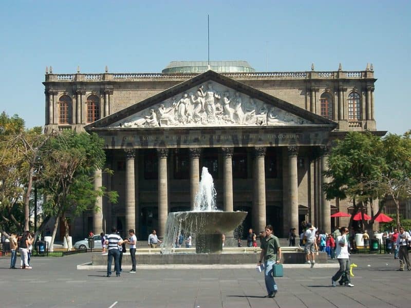 Facade of Guadalajara's Degollado Theater has carvings above its pillars. Fountain in front.