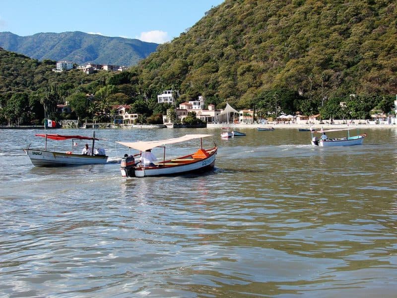 Small motorboats on lake with beach, shops and wooded hills in the background.