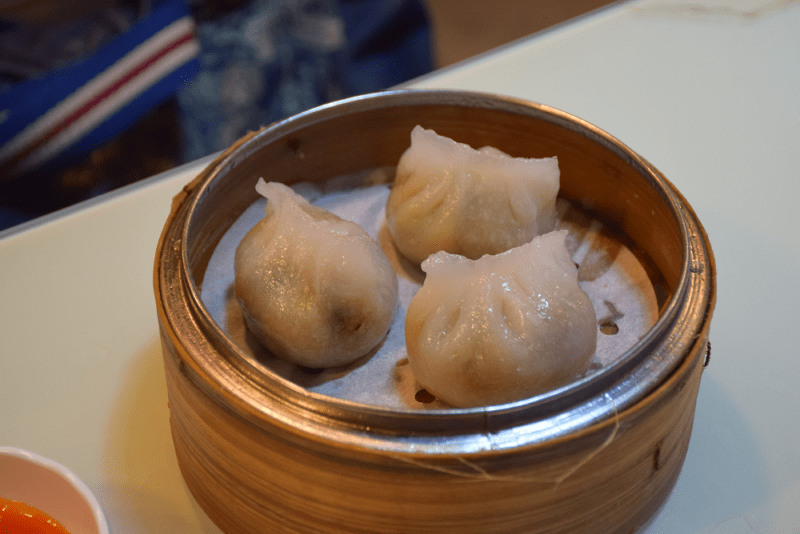 Bamboo tray holding three steamed dim sum, one of the most traditional foods in hong kong