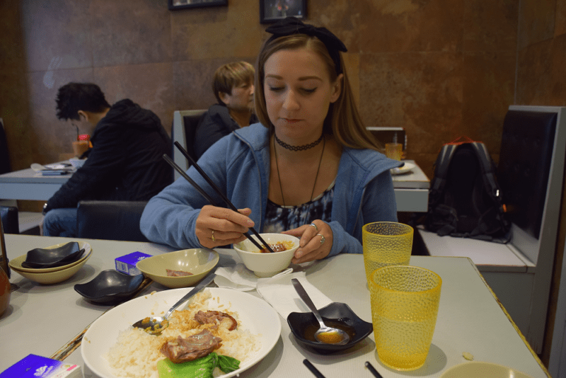 author uses chopsticks to grab a piece of roasted goose in her rice bowl