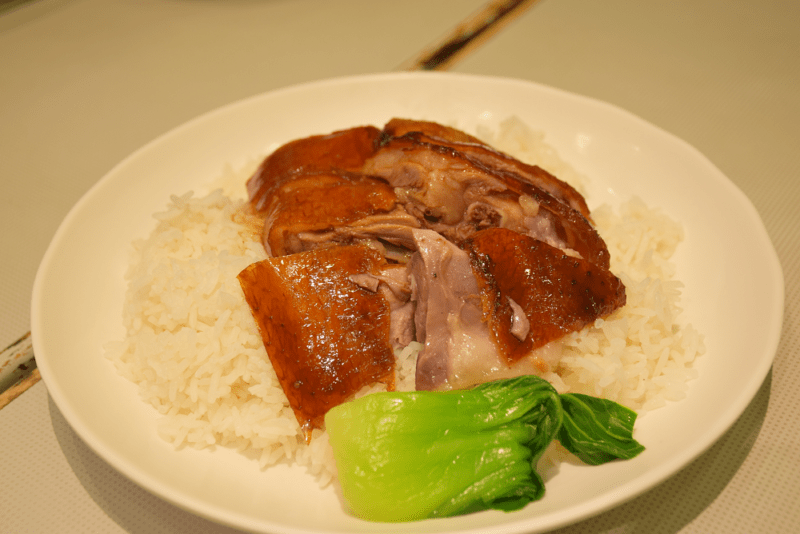 small plate of rice topped with two large slices of roasted goose with skin. 