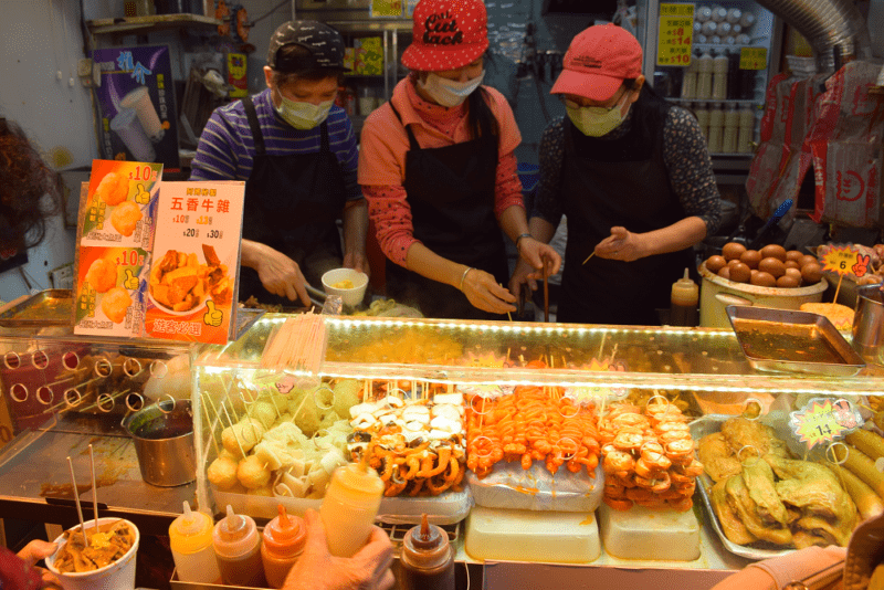 Three staff wear surgical masks as they skewer fish balls behind a counter of food in a Hong Kong restaurant