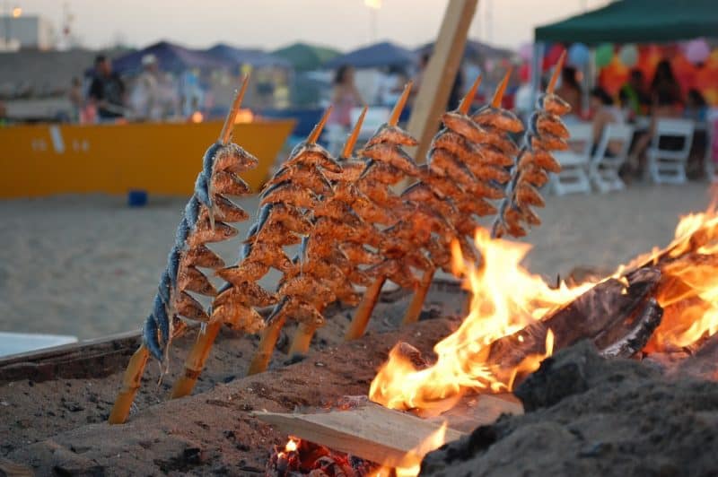 Tall skewers of sardines over an open wood fire on a beach in Costa del Sol Spain