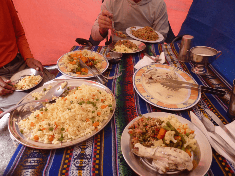 Plates of food on a striped tablecloth. Dinner while hiking the Inca Trail is chicken in creamy sauce, a vegetable medley, quinoa and rice, 