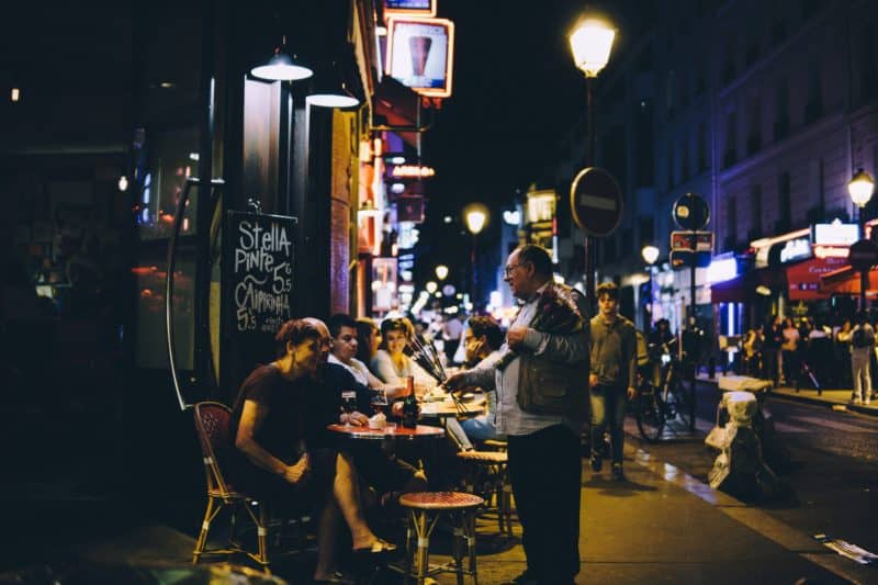 Patrons sit at sidewalk tables enjoying the nightlife