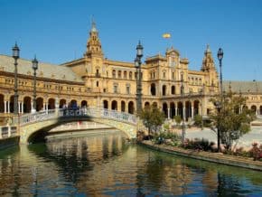 Seville is one of the best reasons to visit the south of Spain. Here, a river and bridge in Plaza de Espana with brick building in background. Spain's flag is flying from the roof.