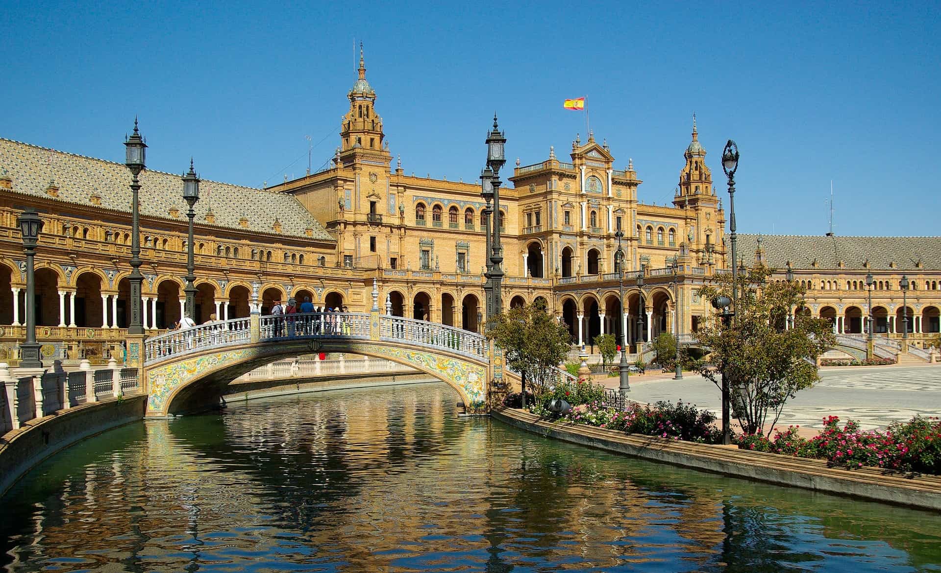 Seville is one of the best reasons to visit the south of Spain. Here, a river and bridge in Plaza de Espana with brick building in background. Spain's flag is flying from the roof.