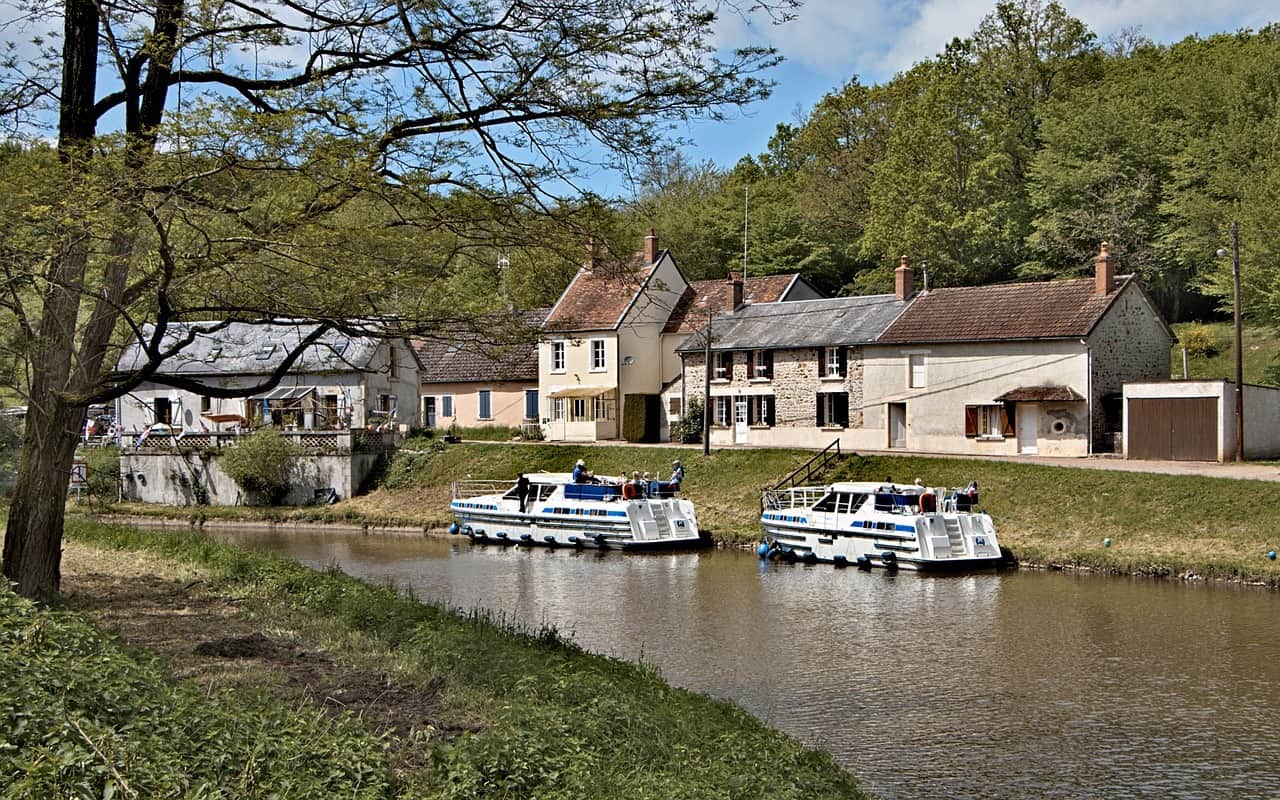 Cruising on a Burgundy canal is one of the most underrated day trips from Paris. This image has two motorboats and a house on the far side of the canal