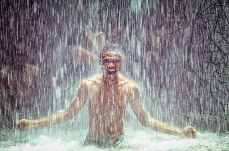 Man under waterfall standing waist deep in water and smiling