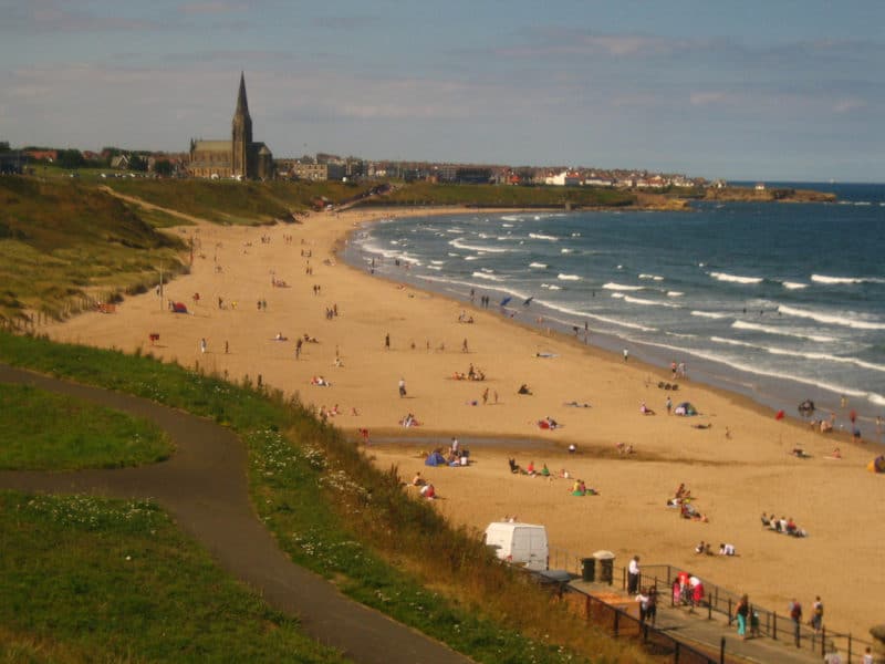 Tynemouth Longsands beach bordered by grass and sea. St. George's Church in distance.