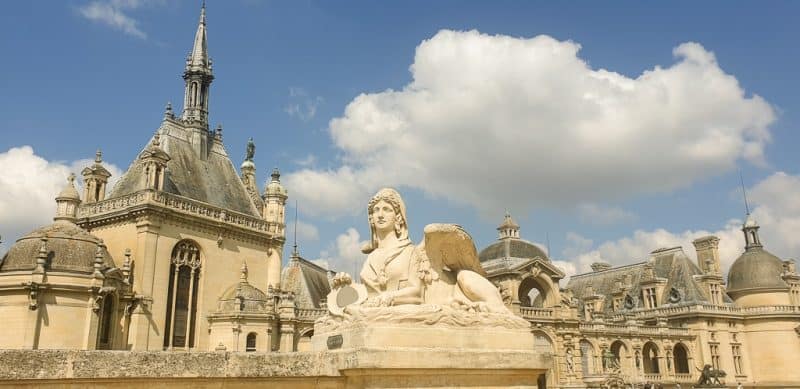 Rooftops of Chateau de Chantilly with sphinx sculpture in the foreground. One of the classic day trips from Paris.