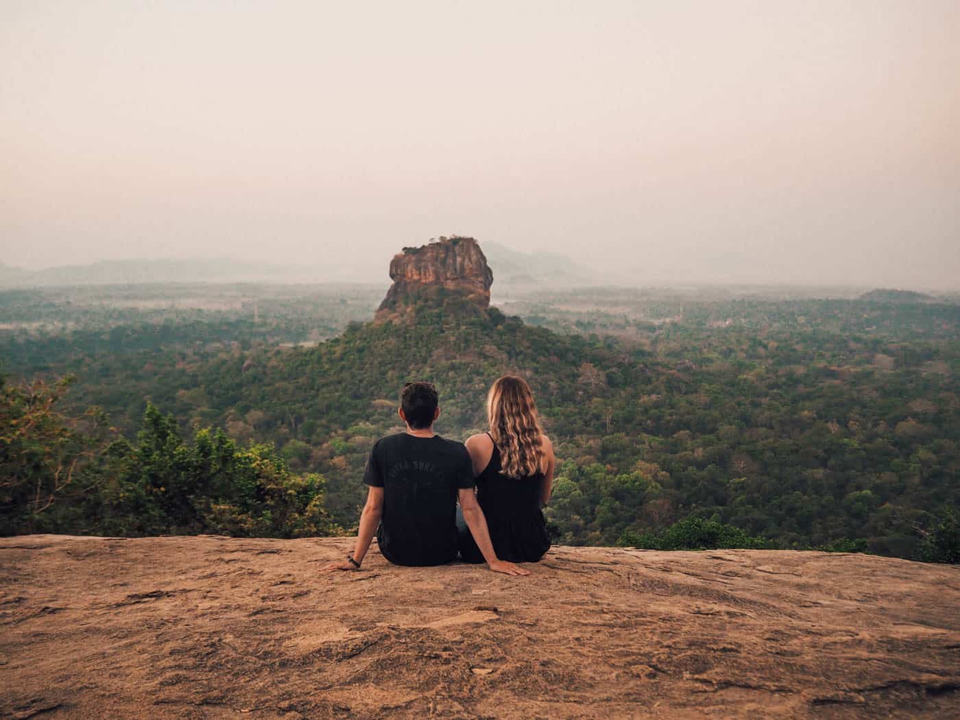 Couple sitting in foreground, with Sigiriya Rock in distance