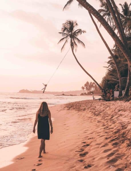 Woman walking toward the palm tree rope swing on Dalawella Beach