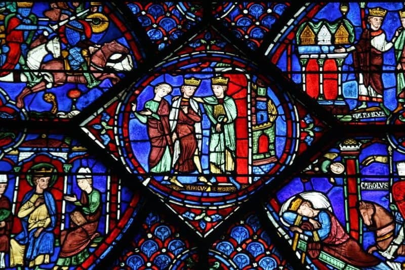 Detail of a stained glass window at Chartres cathedral. Round center image is of two men wearing crowns standing with a woman, and a castle tower in the background.