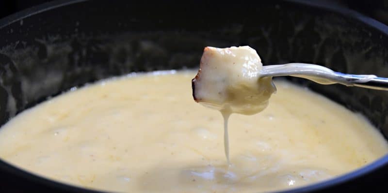 Closeup of a cheese soaked piece of bread dripping cheese back into a pot of bubbling cheese fondue.