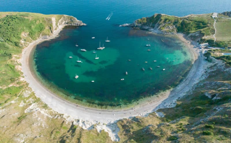Aerial view of Lulworth Cove, with two dozen boats at anchor. This is one of the best beaches on Dorset's Jurassic coast.