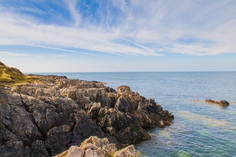 coastal rocks jetting out into light blue waters at whistling sands in wales