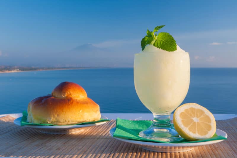 Sicilian lemon granita and a typical warm brioche with blue sea and Mount Etna in the background