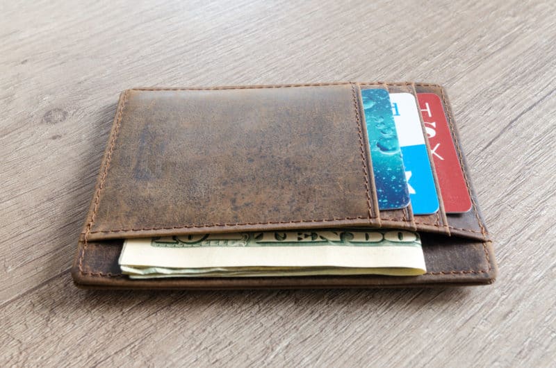 Leather wallet on wooden table with money - be prepared for the cruising add-on costs