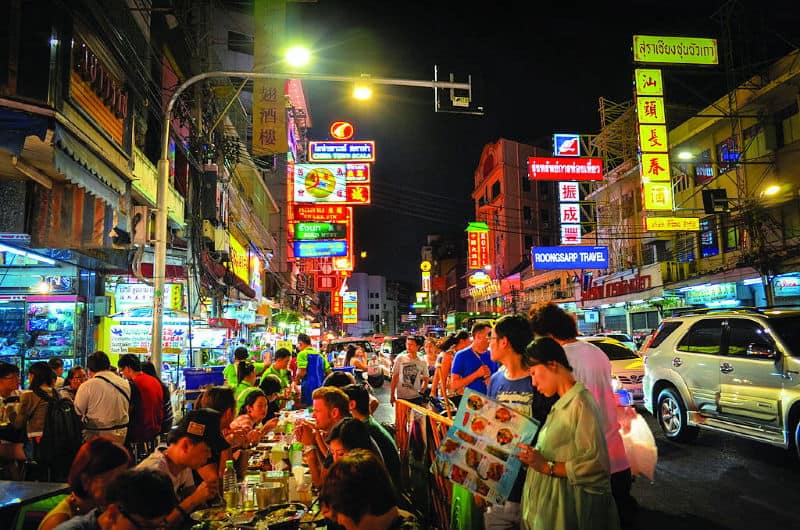 People eating street food on tables on a street in Bangkok's Chinatown