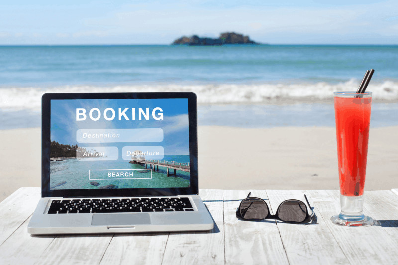 laptop with sunglasses and a drink on the beach. text says booking