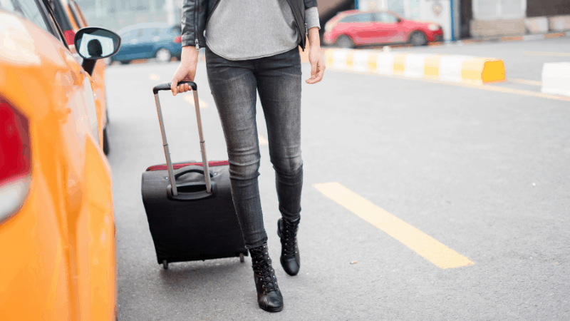 Woman approaching a taxi with a carry-on size bag. Avoid stress when going to the airport by packing everything in one small rollaboard.