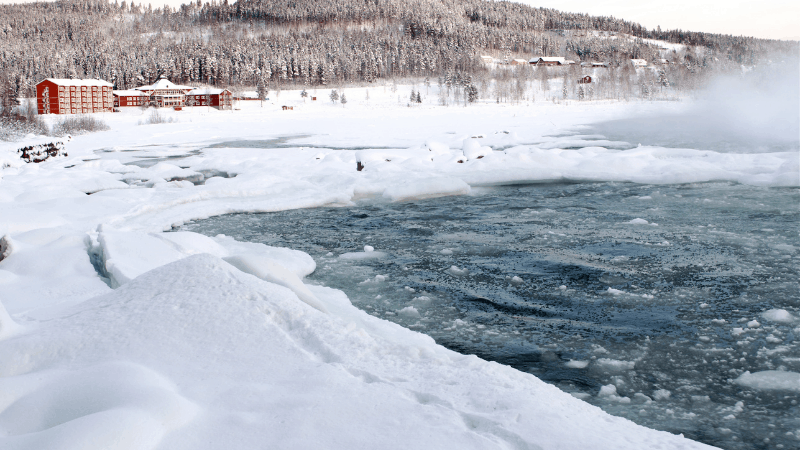 Hotel in Swedish lapland in distance, lake in foreground. Illustrating one of the best destinations in europe in december