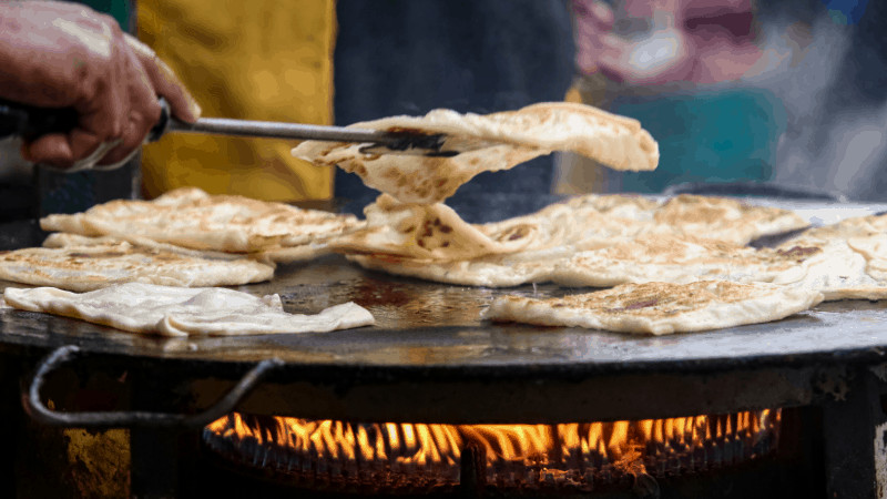 closeup of tongs flipping roti canai