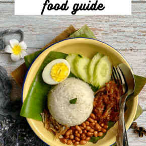 Bowl with a banana leaf, rice, egg, cucumbers, small dried fish called ikan bilis, and peanuts. Text overlay says "Penang food guide"