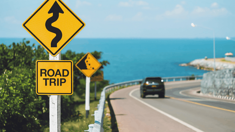 Road trip sign, car on a road, ocean in background