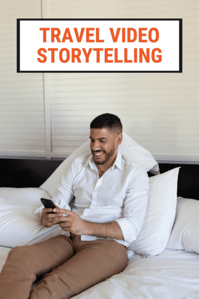 Man holding a phone while sitting on a bed. Text overlay says "travel video storytelling"