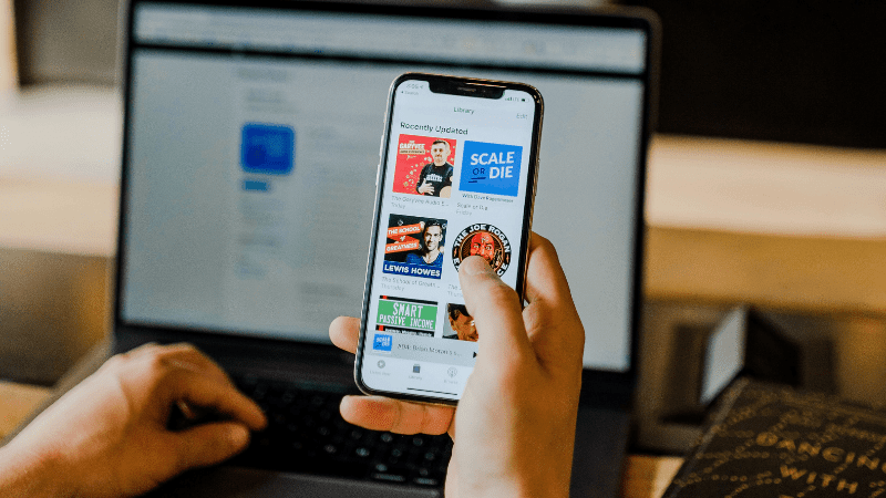 hand holding phone with podcasts. Syncing with computer in background