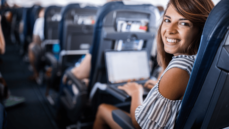 Woman smiling at camera while using computer on a plane