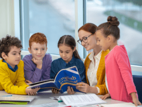 Woman teaching English to children standing around her