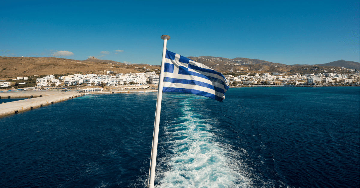 Greek flag on the back of a boat. The wake from a boat motor leads back to shore. Best greek islands to visit.