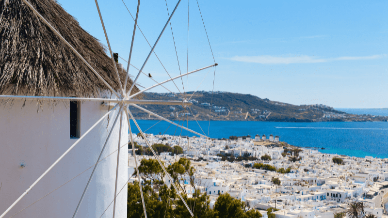 Windmill on the Greek island of Mykonos, village, water and hill in background.