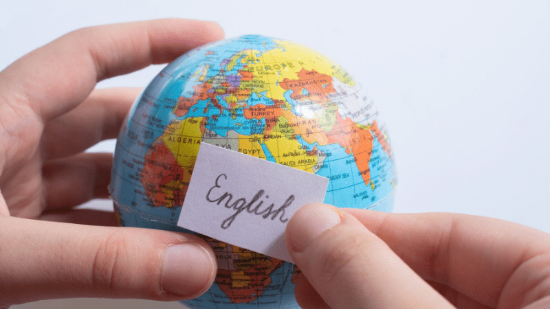 hand holding a small globe. Another hand holds a small piece of paper that says English on it. Illustrating teaching English overseas
