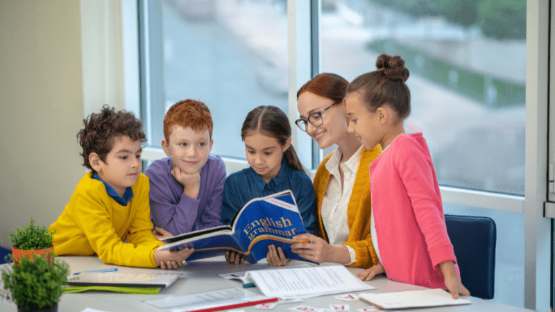 Woman teaching English as a second language to children standing around her. She has a tesol certificate.