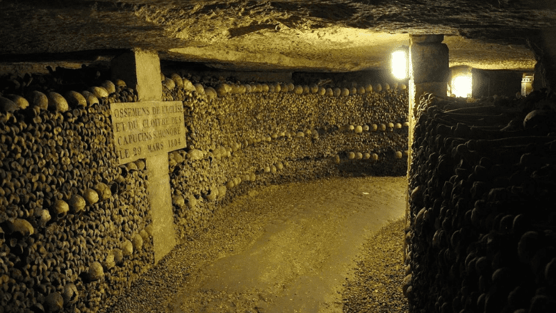 Cross and passageway lined with bones in the catacombs of Paris
