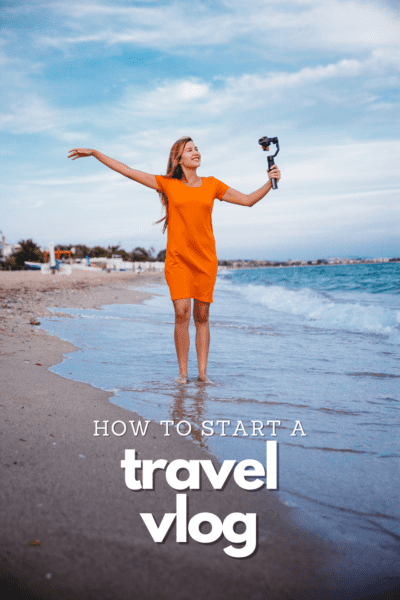 Woman photographing herself on a beach. Text overlay says "how to start a travel vlog"
